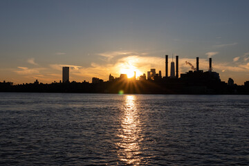 Naklejka premium Bright Sunset and the Manhattan Skyline Silhouette with Smoke Stacks along the East River in New York City