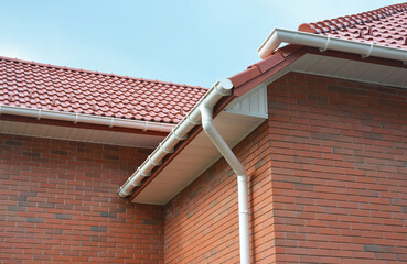 A close-up on plastic rain gutters, downspout, soffit and fascia with a box-end on the corner of a...