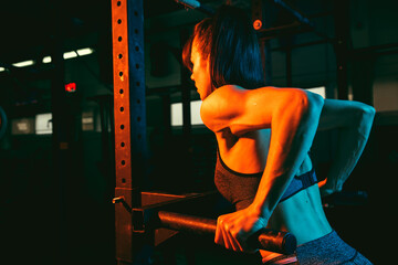 Young athletic woman, fitness instructor training in gym in mixed neon light.