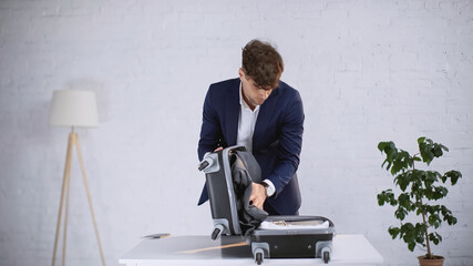 businessman in suit closing packed suitcase at home