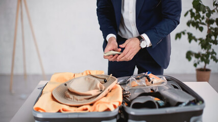 cropped view of businessman in suit holding money while packing luggage