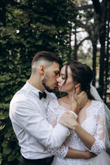 Walk of the bride and groom in the summer park. Newlyweds in seclusion. He and she against the backdrop of green foliage.