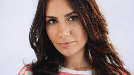 close up of brunette woman looking at at camera near white brick wall