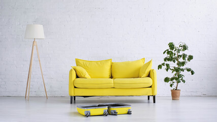 yellow sofa near floor lamp, plant and suitcase on floor