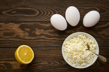Bowl with cottage cheese, chicken eggs and lemon on a wooden table, flat lay
