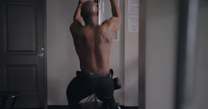 Black man using lat pull down machine to weight train in gym, View from Behind
