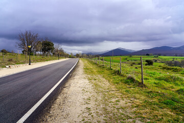 Fototapeta na wymiar Asphalt road leading to mountains with dark storm cloud sky.