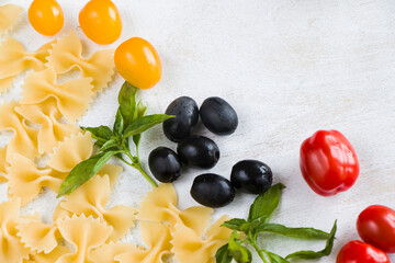 Pasta ingredients, raw pasta, cherry tomatoes, olives and basil leaves