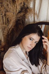 Obraz premium Beautiful stylish woman in suit sitting on retro wooden chair in bohemian style room with dry grass