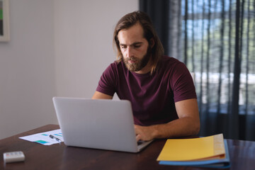 Caucasian man sitting at table working from home and using laptop