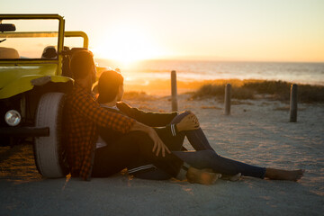 Happy caucasian couple leaning against beach buggy by the sea watching sunset