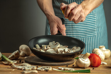 A chef in a blue apron is squeezing lemon juice into mushrooms in a frying pan. Concept of process cooking food