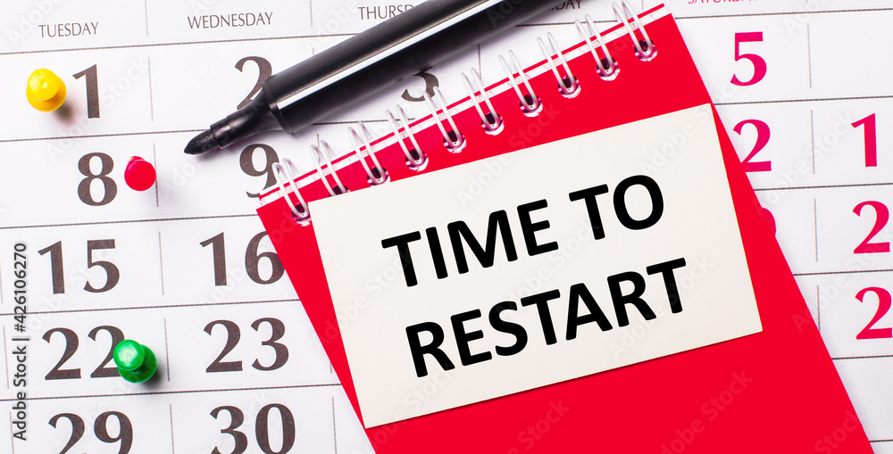 Poster on the calendar is a white card with the text time to restart. nearby is a red notepad and a marker.