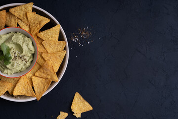Avocado hummus dip and corn chips on dark gray table, top view
