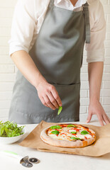 chef puts green basil leaves on the pizza