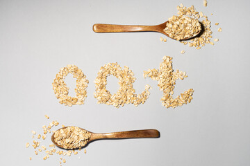 Word OAT made of flakes and oat on wooden spoon on grey background