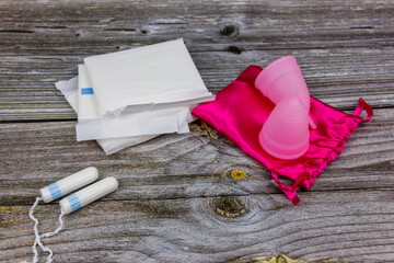 Sanitary pad, tampons and menstrual cup on wooden background. Concept of critical days, menstruation, feminine hygiene