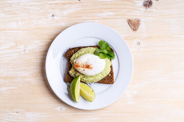Rye bread avocado hummus toast with poached egg on white plate