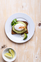 Rye bread avocado hummus toast with poached egg on white plate