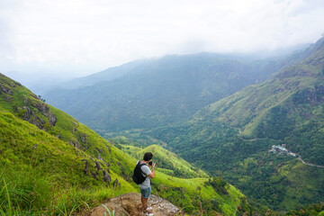 Naklejka na ściany i meble Young man taking pictures of a huge valley in mini Adams Peak, Sri Lanka.