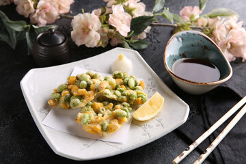 Japanese cuisine. Vegetables, green peas in tempura on a white plate on a black table with soy sauce. Restaurant menu. Background image, copy space
