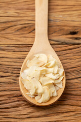 Closeup of dried garlic slices on a wooden spoon. Food backdrop