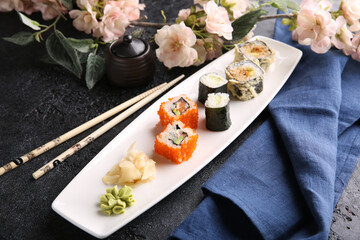 Japanese cuisine. Assorted rolls and sushi with ginger on a white plate on a black table with soy sauce. Chopsticks, sakura. Restaurant menu. Background image, copy space