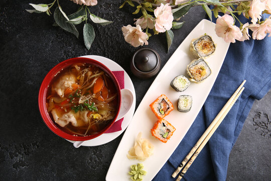 Japanese cuisine. Assorted rolls and sushi with ginger with soup in bowl on a white plate on a black table with soy sauce. Chopsticks, sakura. Restaurant menu. Background image, copy space