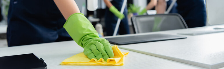 Cropped view of cleaner cleaning table with rag in office, banner