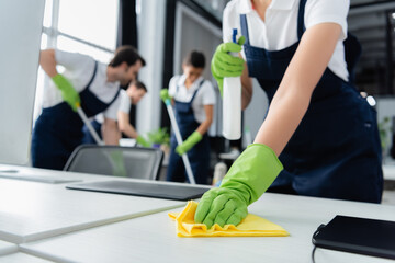 Rag in hand of cleaner holding detergent near table in office