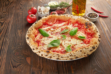 Original italian neapolitan pizza Margherita with melted mozzarella cheese, fresh basil leaves and tomato sauce on wooden table with ingredients. Fast food italian menu and vegetarian eating concept