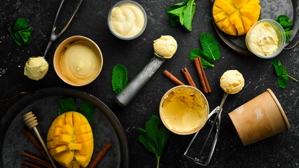 Mango ice cream with mint and fresh mango. Ice cream spoon. On a black stone background, top view.