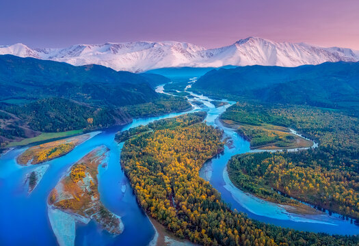 Autumn view of the river bed with shallows of yellow trees after sunset against the background of high mountains, the Abakan river in Khakassia