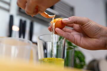 Breaking an egg into a container. Preparation of an Italian dish. Visible hands.