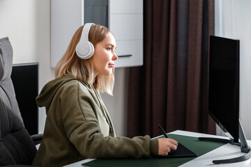 Young woman graphic designer freelancer busy working remote from home using pc computer and graphics tablet in living room interior. Casual teenager girl in draws studying animation and visual arts.