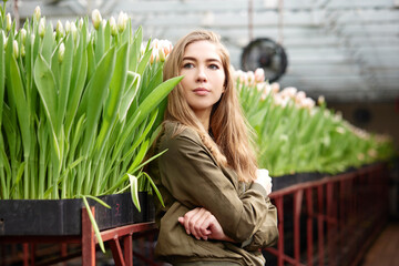 Young woman in green dress stands looking at flowers in a greenhouse Tulips