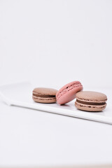 Obraz na płótnie Canvas three pink and brown macaroons laying on the white plate, copy space