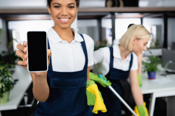 Smartphone in hand of african american cleaner on blurred background in office