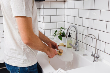 A man washes dishes in the kitchen with a wooden eco brush