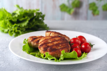 Fried cutlet with salad and tomatoes in a white plate on a gray background