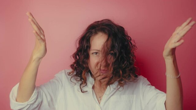 Angry irritated young woman in white shirt isolated on a pink background. Looking at camera spreading hands put palm on head and hits herself on the head