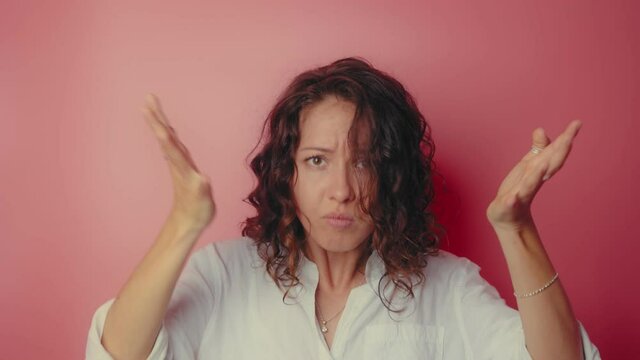 Angry irritated young woman in white shirt isolated on a pink background. Looking at camera spreading hands put palm on head and hits herself on the head