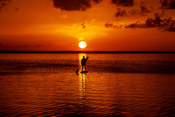 Stand up paddling into the sunset on the sea / ocean