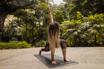 Caucasian woman with blonde dreadlocks in yoga pose on a black mat