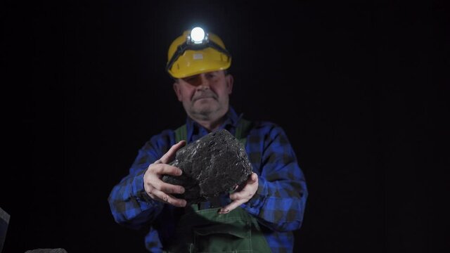 A miner turns a large lump of black coal in his hands. Close-up view