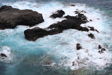 Turquoise ocean waves crashing against the rocks. Bird's eye view of the ocean water, from above.