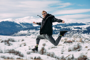 Young joyful man jumps against beautiful landscape of mountains and sky.