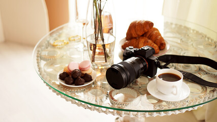 Photo camera with a lens on glass table. Cup of coffee, macaroons and croissants