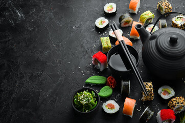 Background of sushi rolls with tea, ginger, wasabi and soy sauce on a black stone background....