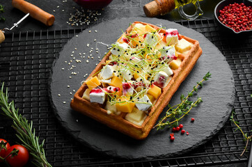 Breakfast. Belgian waffles with brie cheese, feta and parmesan. On a black stone plate.